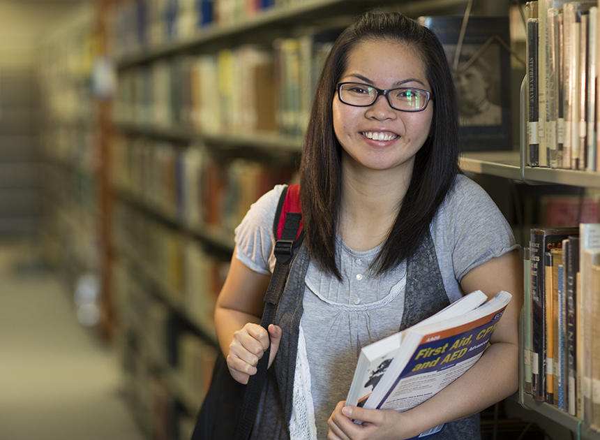 CCBC student stands in front of a book shelf in the library