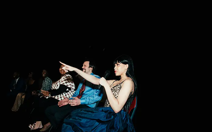 A woman speaking into a microphone and pointing at the audience.