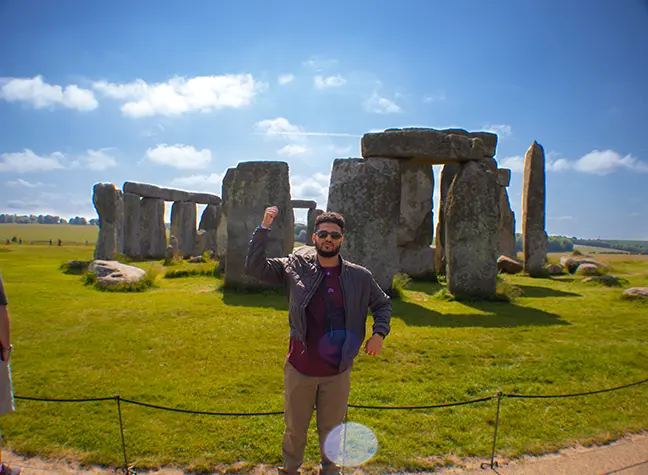 A student waving at the camera in front of Stonhenge.