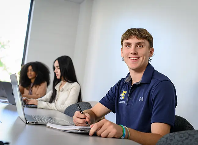 A student takes notes as he works on his laptop.