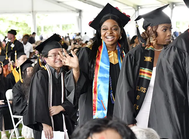 A student waves to the camera as the graduates line up to exit the Commencement tent.