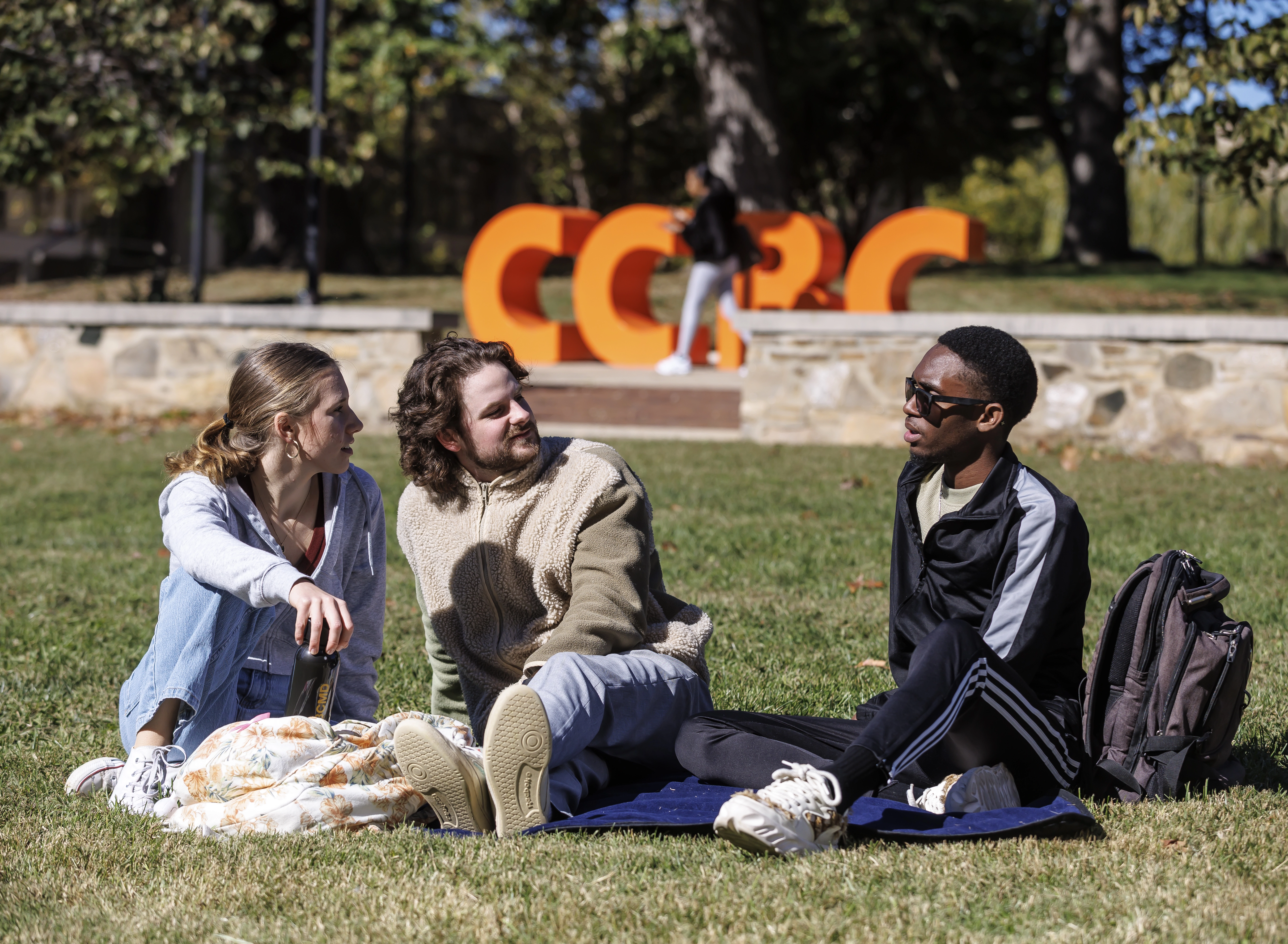 Three students sit together on a picnic blanket in the quad, enjoying a sunny afternoon at CCBC.