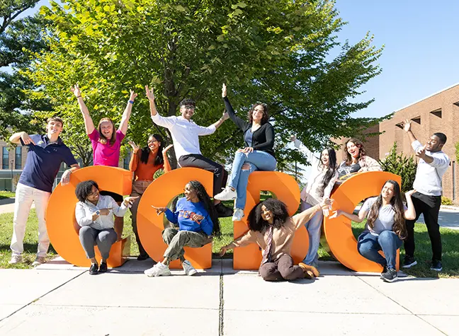 A group of students sit around large orange letters that read, "CCBC."