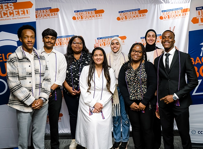 A CCBC graduate stands on the Commencement stage holding his diploma.