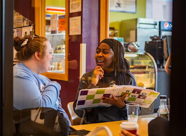 Two students sit outside of the Cafe going over the contents in a binder.