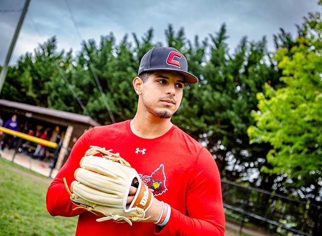 A CCBC cardinals baseball player holding a baseball in his glove.