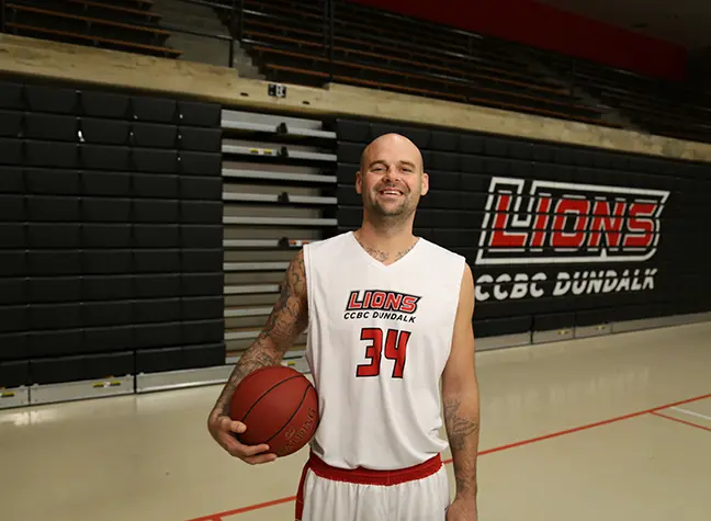 CCBC Dundalk Lions men's basketball player in uniform holding a basketball in the gymnasium.