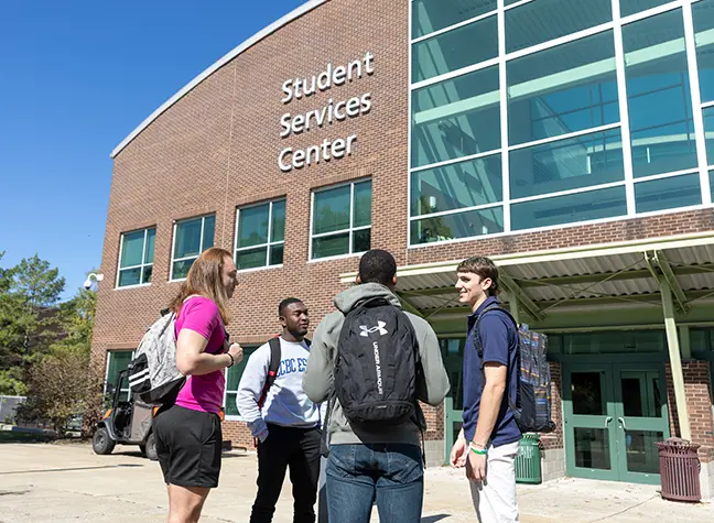     Four students gathered outside of a building that reads "Student Services Center." 