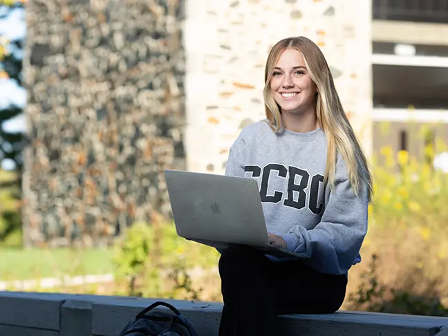 CCBC student on her laptop sitting in front of the Math and Science building