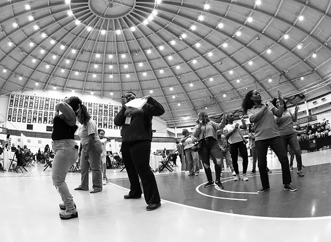 A group of students with their friends and families dancing in the gymnasium.