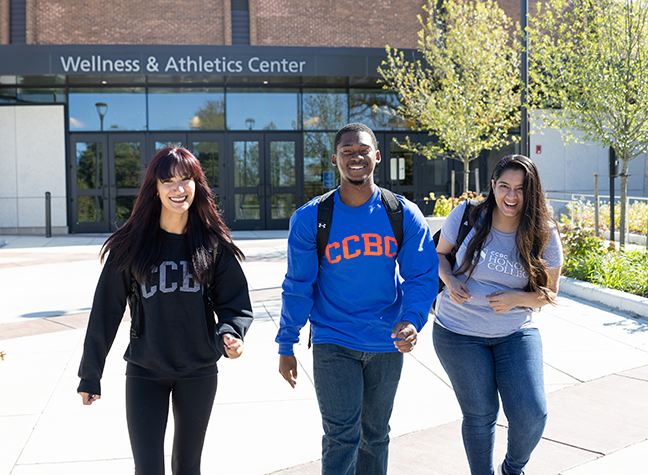 Three students walking in front of a building that reads "Wellness & Athletics Center." 