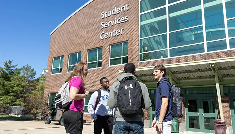 Four students stand in a circle outside of the Student Services Center on the CCBC Essex campus.