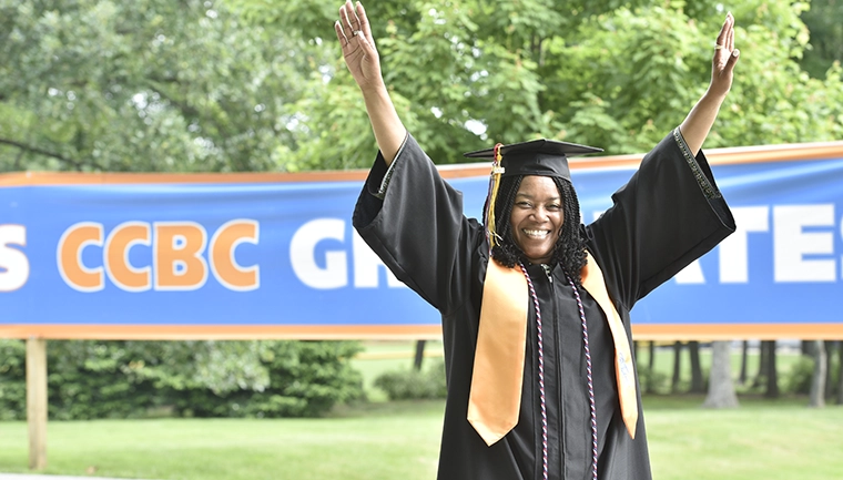 Graduate students outside with her hands in the air, smiling.