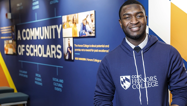 honors student wearing an honors college hoodie, stands in front of CCBC honors college wall art.