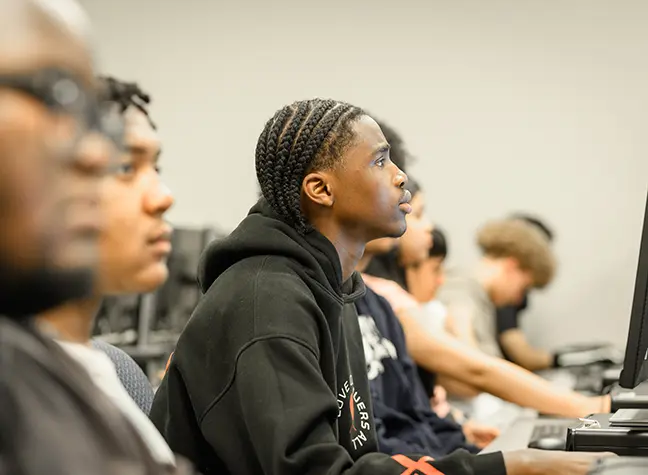 A student focused and working on the computer in front of him.