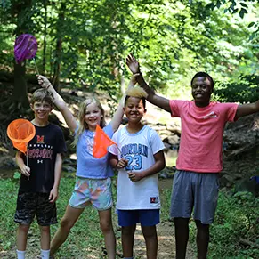 A Camp Heritage staff counselor (right) standing next to three campers holding butterfly nets.