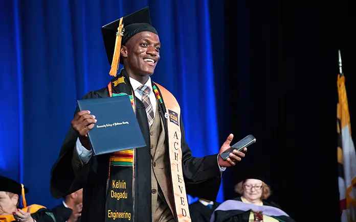 Kelvin Dagadu walking across the commencement stage with degree in hand.