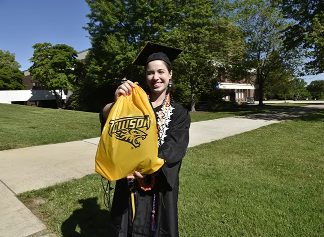 Photo of a student with a cap and gown holding a Towson Tigers bag.