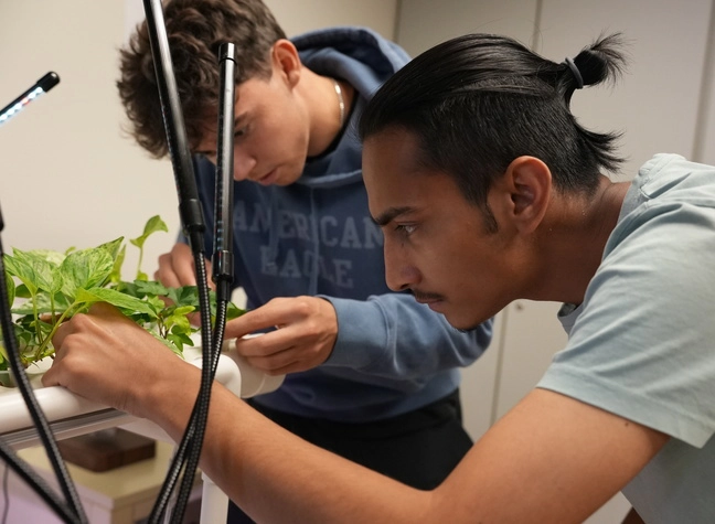Two younger students observing plants in a lab