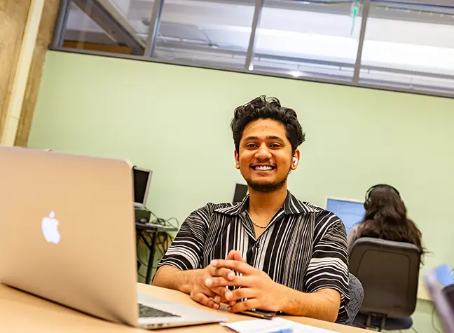 A student working on his laptop in a bright classroom.