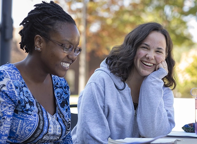Two female students sitting outside laughing