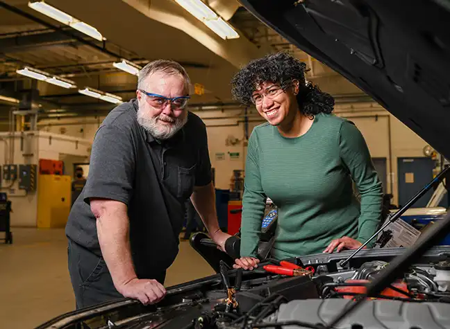 Two students working under the hood of a car in our automotive lab