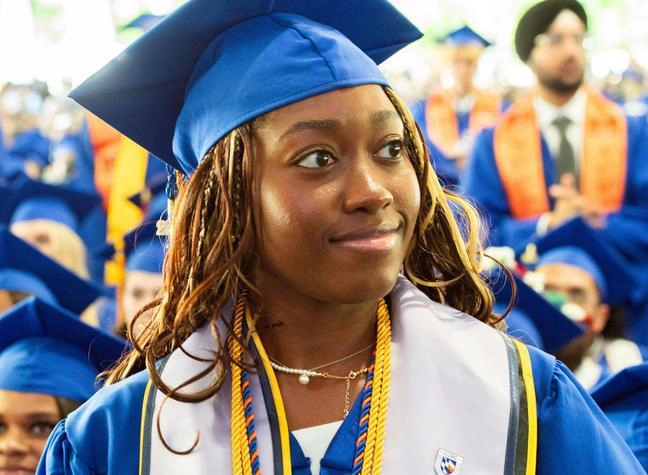 CCBC graduate wearing cap and gown, holding a proud to be CCBC sign