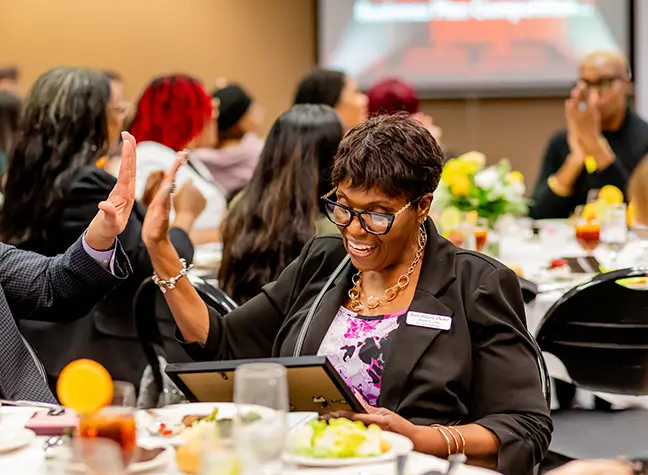 Owner of Alumni Showcase winner, Events U Love, looks at her award and high-fives the man sitting next to her at the event table.