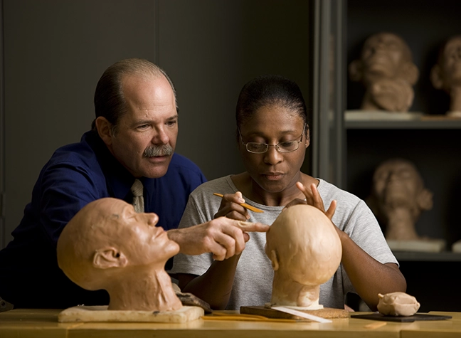 Mortuary science faculty assists a student who is sculpting a clay head