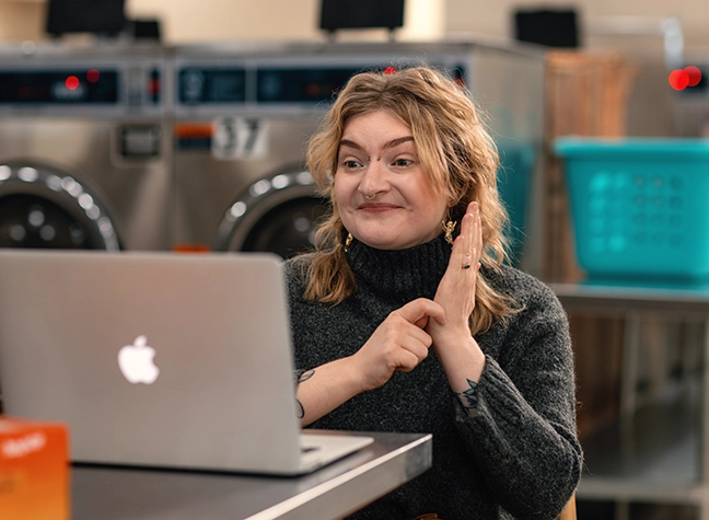 ASL student performs sign language in front of laptop