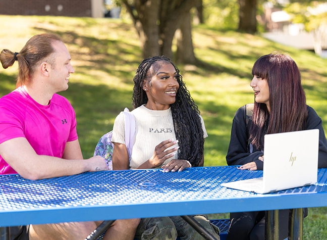 Three students outside on a sunny day with a laptop