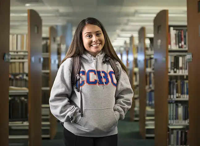 Female student wearing backpack standing in the library