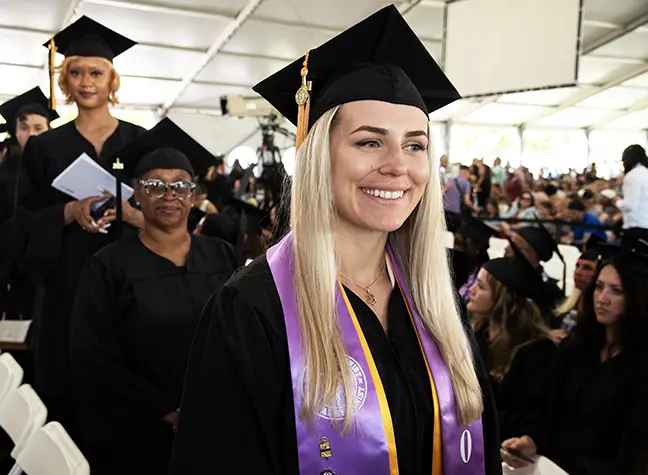 A graduate smiling as she lines up to leave the Commencement Ceremony tent.