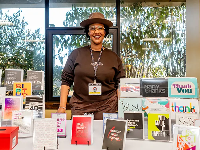 A small business owner of a stationary brand stands behind a table full of her creations.