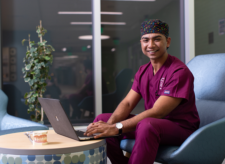 Dental student sitting in lounge chair with laptop.