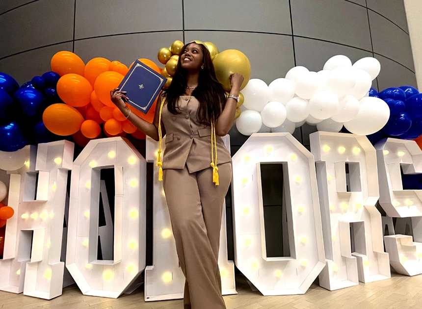 Woman with diploma in front of balloons and display that says "Honors"
