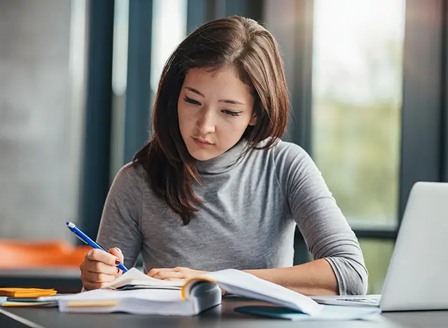 Young woman takes notes while studying in the library.