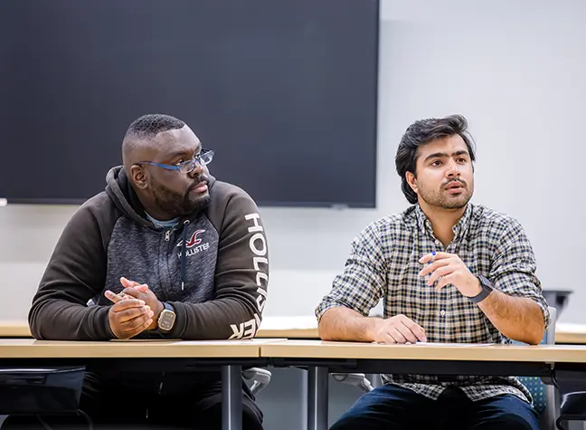Two students sitting next to each other at a desk in a classroom.